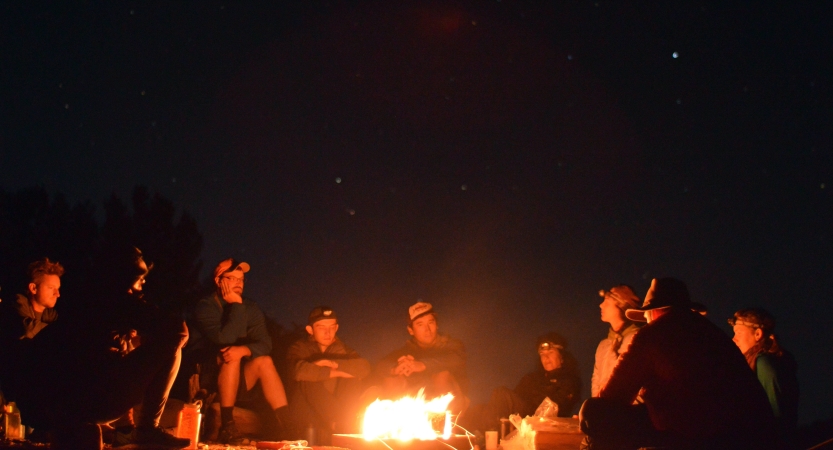 A group of people sit around a campfire. 